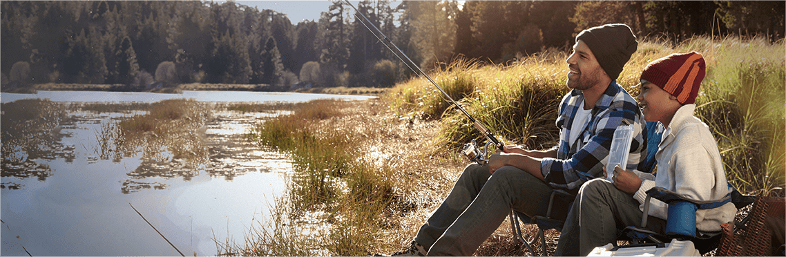 A father and son sitting near a pond holding a fishing rod